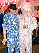 A male burner in a blue paisley pajamas and black fedora embraces another male burner in pink patterned pajamas and a pink furry top hat.