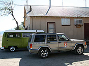 A Jeep-brand SUV, branded KTVN-RENO, is parked beside an old VW bus outside Burning Man's Gerlach office.