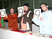Three male judges hold up cards announcing their scores.  The leftmost, wearing a tiger costume (sans head), holds an upside-down '10.'  The second, in winter attire, offers a '9.'  The third, in a pale blue fur suit, also offers a '9.'