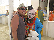 Near the sales counter, a man wearing a fedora poses with a clown holding a teddy bear.