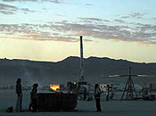 Three participants approach a burn platform fire at dusk.