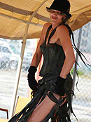 A woman models an all-black ensemble including a derby, corset and ribbon skirt.