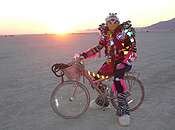 A costumed burner poses alone on his bike in front as the sun peeks over the horizon.