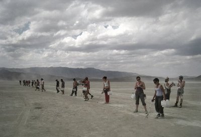 a line of people spread across the playa carrying buckets preparing to perform a line sweep