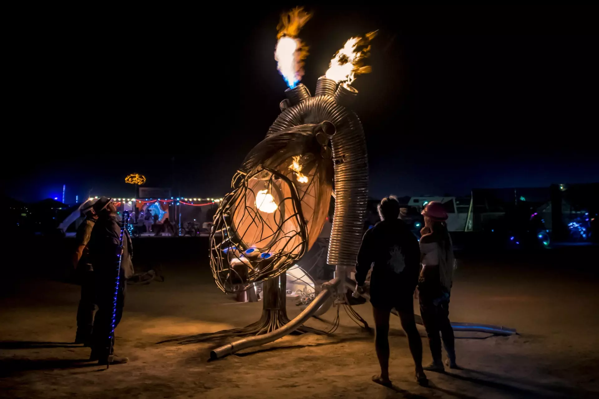 Giant metal anatomical heart sculpture with with flames shooting out the aortas at night on playa