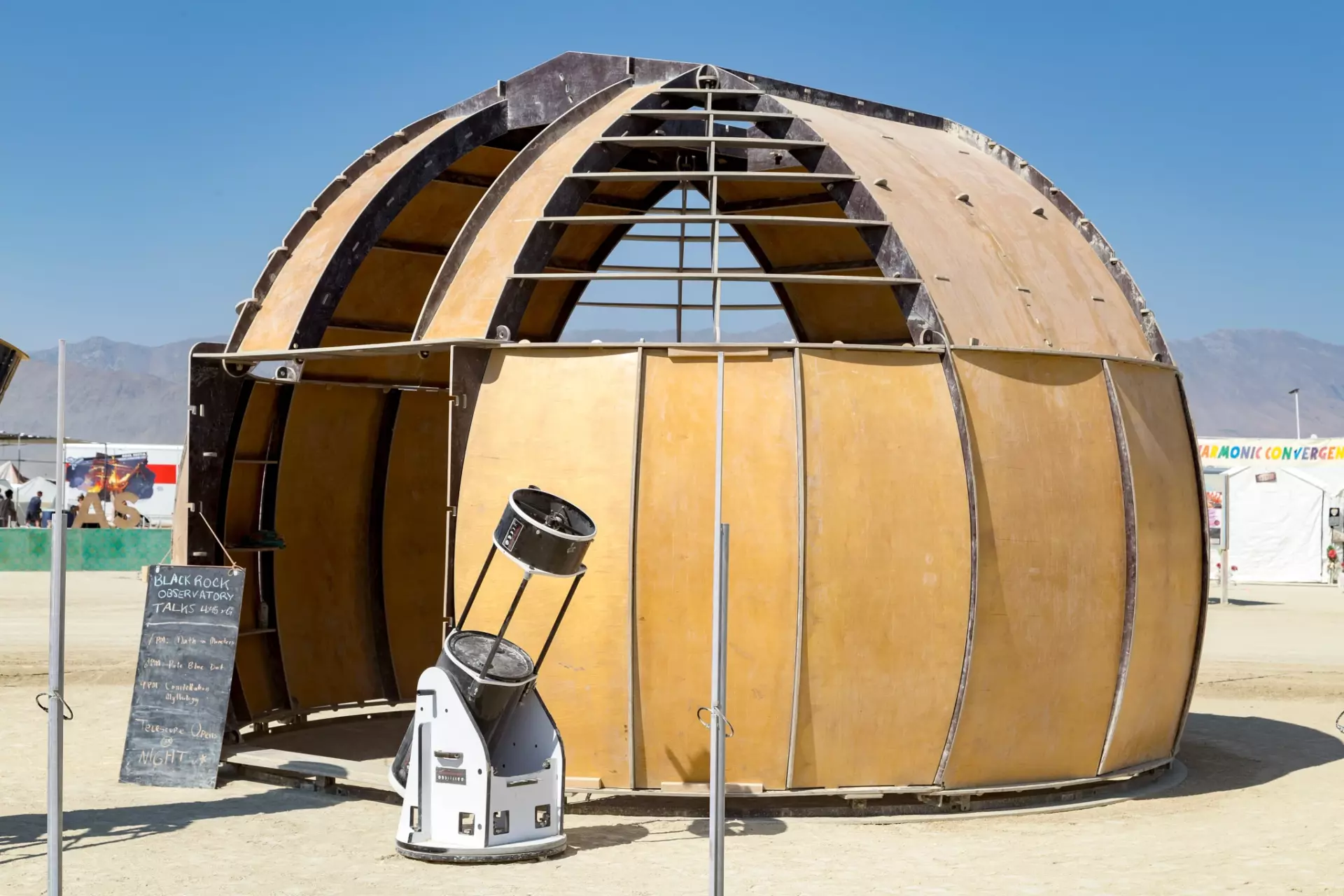 Round domed wooden structure on playa during the daytime with a real telescope outside