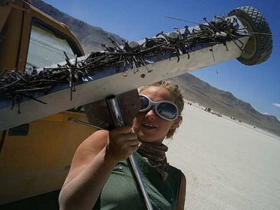 woman on playa in googles holding up a magnet sweeper tool with many pieces of metal MOOP magnetized to it