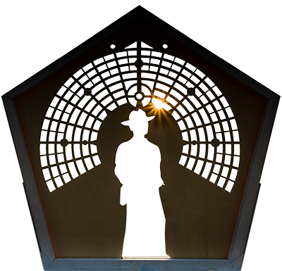 Metal sculpture, a pentagon with the city map in an arch over a cutout of Larry Harvey's full body profile. The sunset glints through 1:00 at Esplanade.