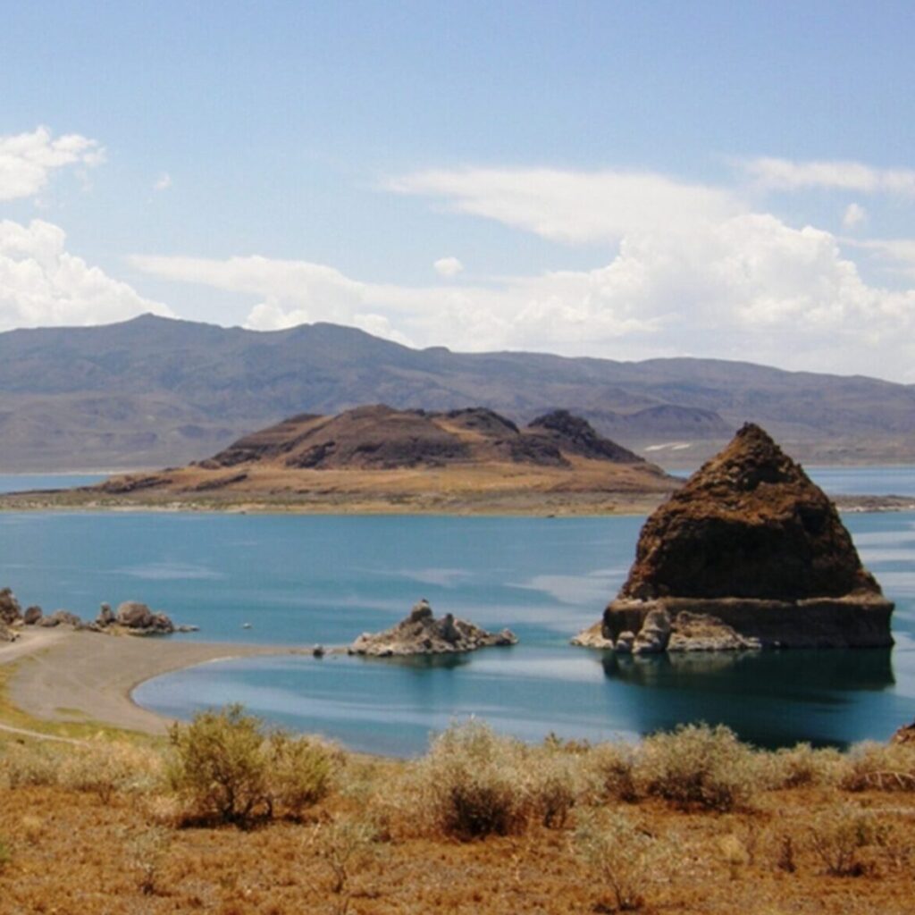 The shoreline of Pyramid Lake in the foreground, the lake and pyramid in the background.