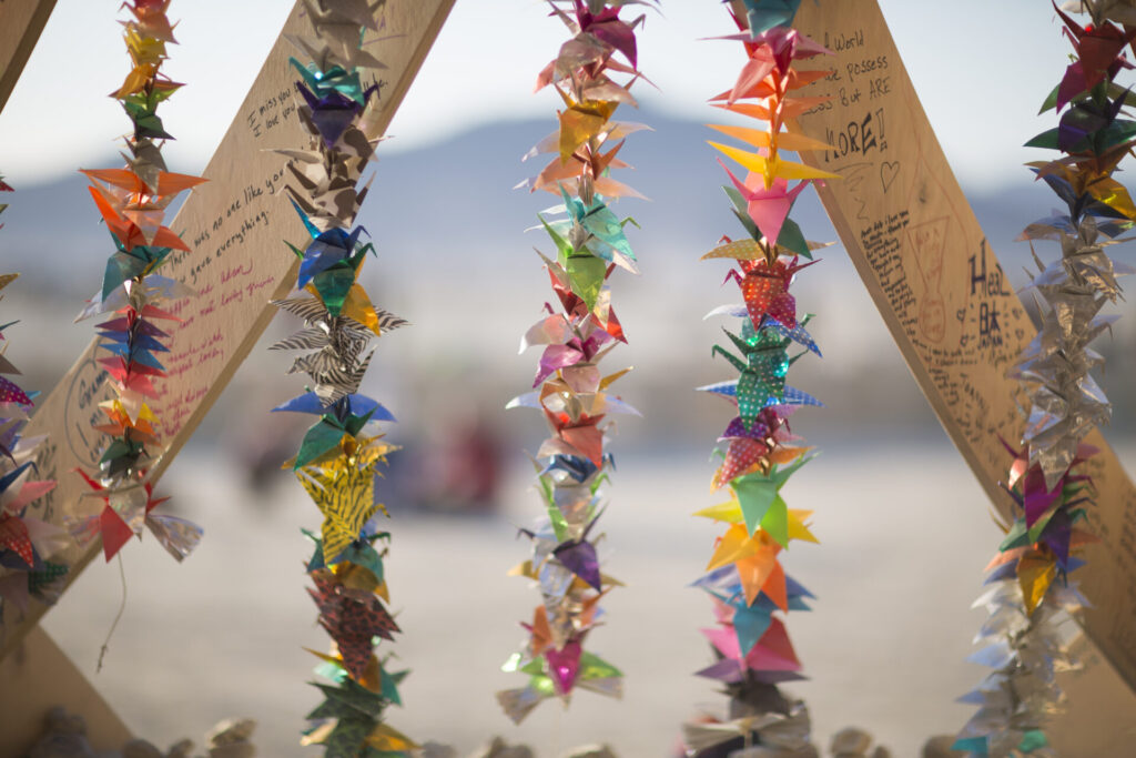 Paper cranes are strung on lines and hung from wood bars.