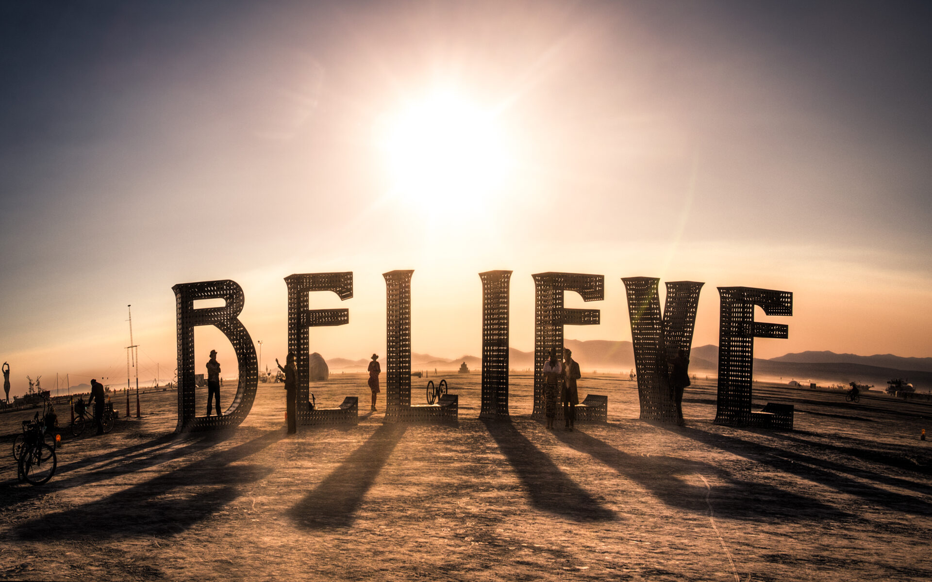 Large metal letters spell out the word "believe", with sun setting in the background.
