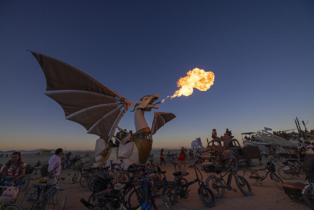 Dragon mutant vehicle breathes fire into the night sky, surrounded by bikes.