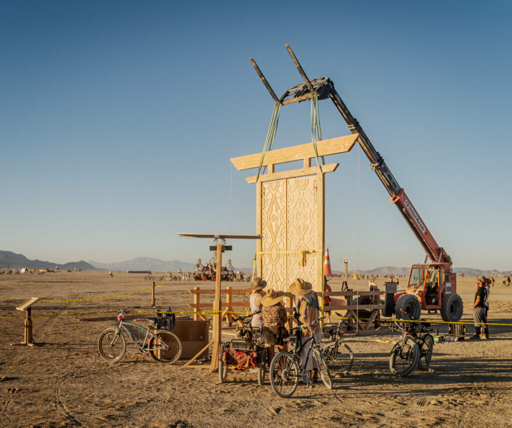 Large construction machine hoisting up a wooded gate at Black Rock City. 