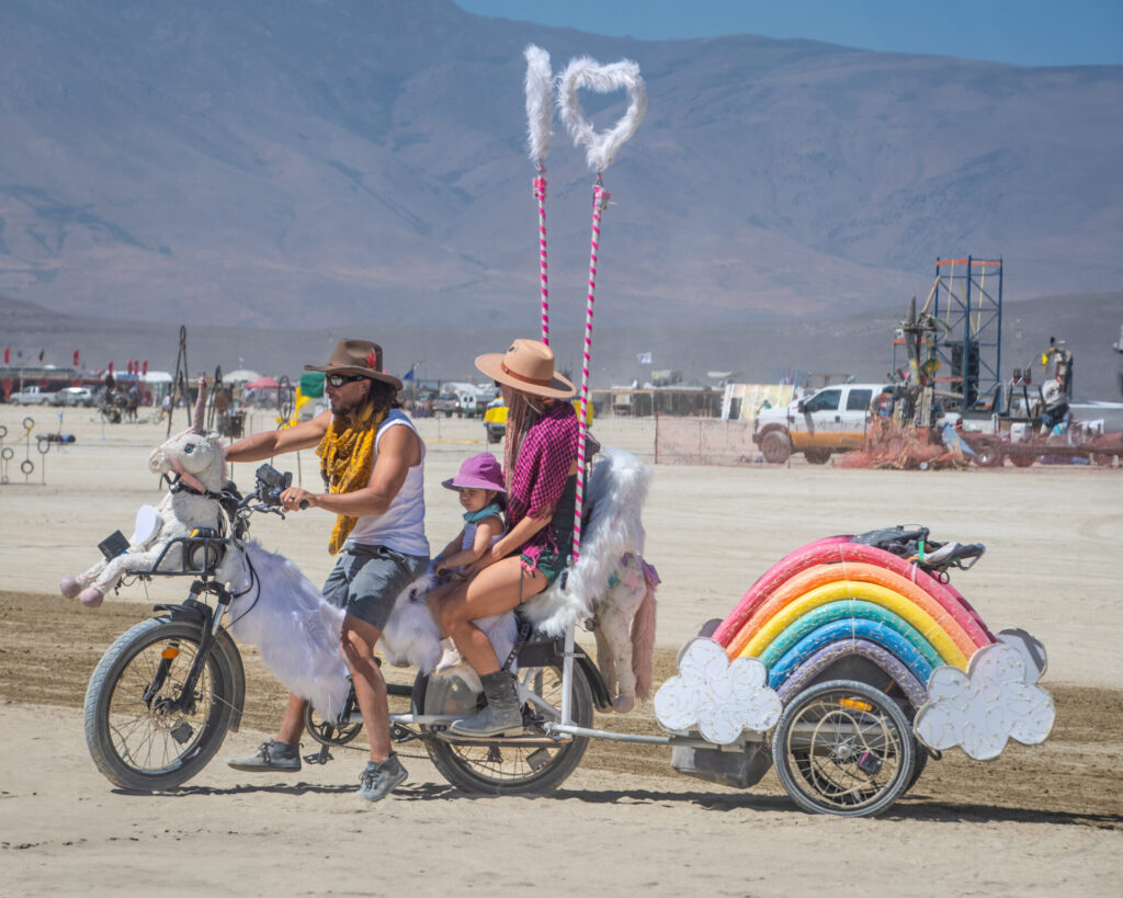 Family riding a bike decorated with a rainbow at Black Rock City