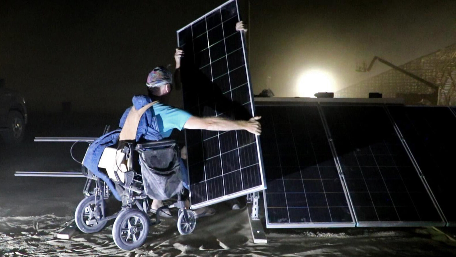 Person in wheelchair installs a solar panel at night
