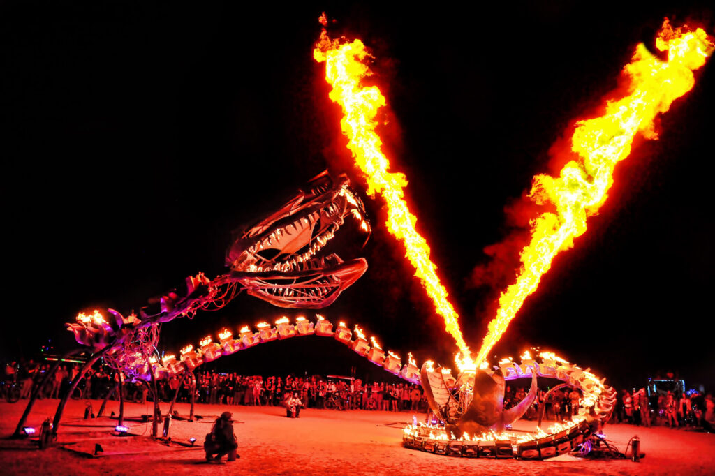 A metal serpent wraps around an egg that is shooting two steams of flaming methanol into the air. Serpent Mother, by Flaming Lotus Girls