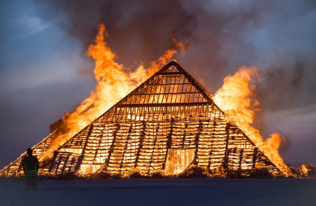 A pyramid engulfed in flame with a person standing at the base