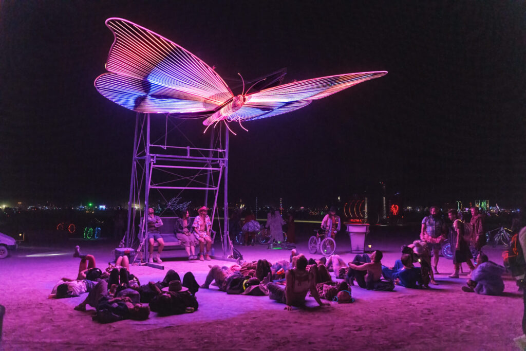 An LED butterfly suspended over the heads of people lying on the ground.