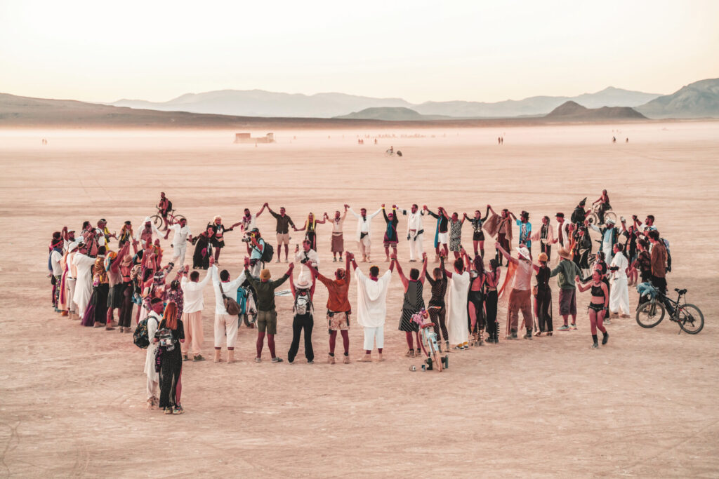 A large circle of burners raise their hands in celebration of a couple's playa wedding