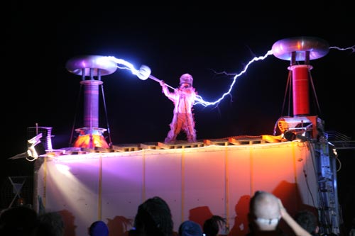 A man stands between two tesla coils as lightning bolts from each hand to the coils.
