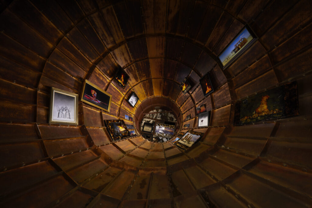 A wood-paneled tube with photos and drawings hung on all sides.