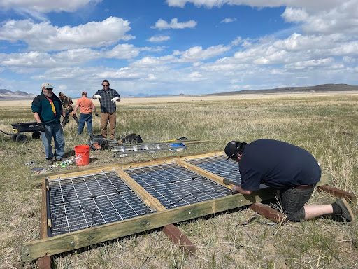 A man assembles three solar panels in a wood frame in a field at Fly Ranch