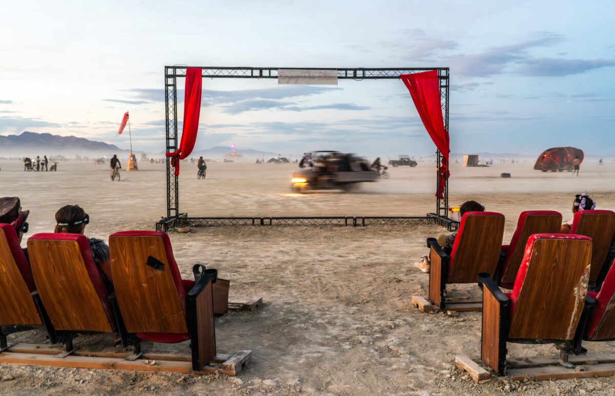 A stage with a view of the playa, framed with curtains and a sign that reads Enjoy the Show, in front of theater seats