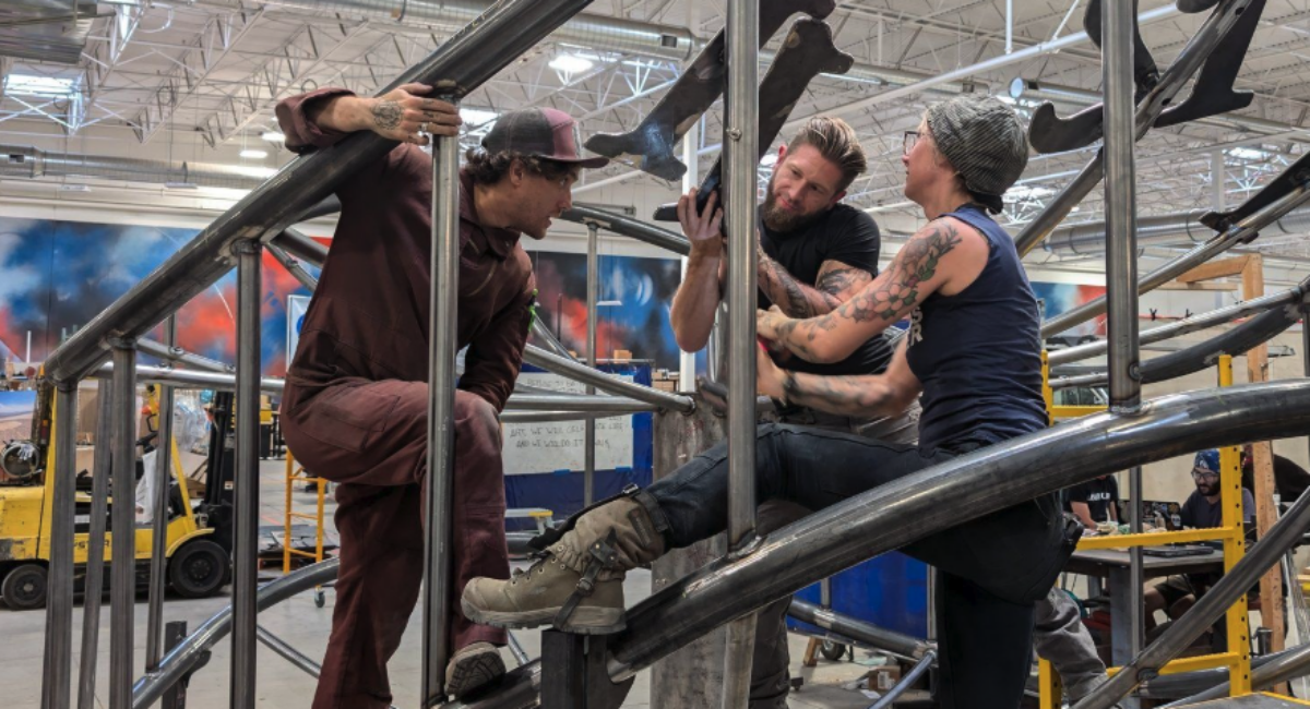 Three people balance heavy metal numbers as they assemble a giant clock