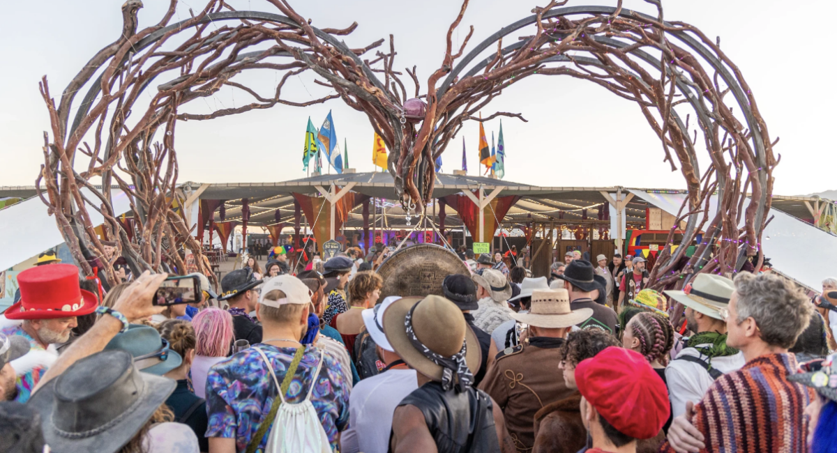 A group of people stand below tree branches shaped into a heart, at the edge of Center Camp.