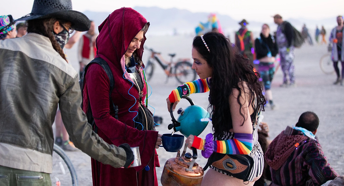 A woman carrying tea pots pours beverages for other participants at dawn.