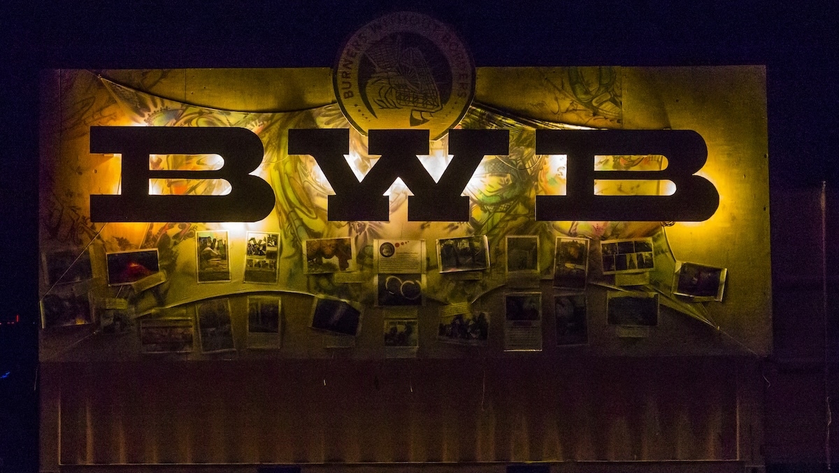 Decorative banner hung on a shipping container with BWB letters lit from behind and photos of members