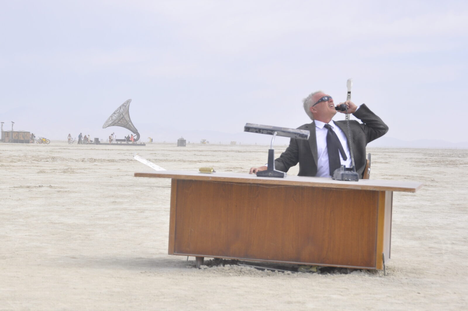 Man in suit at a desk on playa, holding phone to his ear