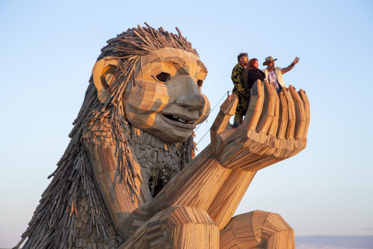 Troll statue made of wood, hands raised to a cup in front of its face.