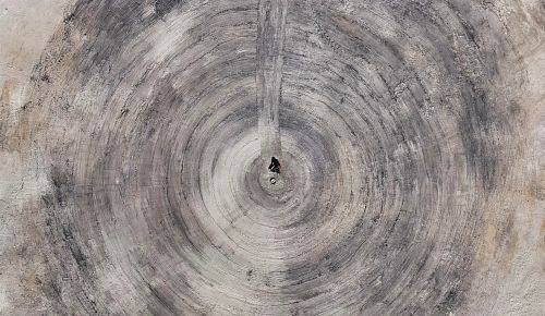 Aerial view of the ashes from the temple, raked into a spiral with artist seated in the center.