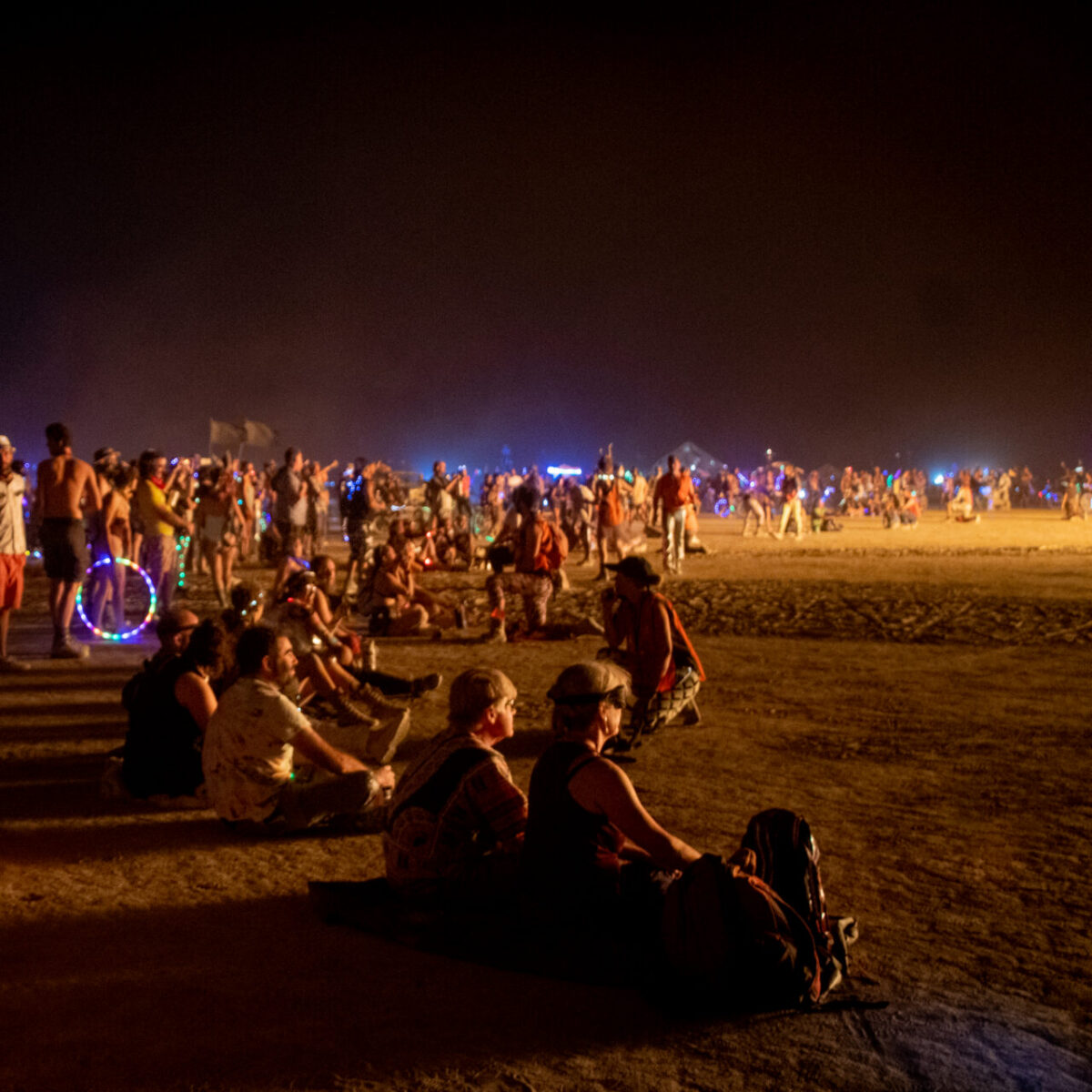 People sit in a wide circle bathed in the glow of a fire