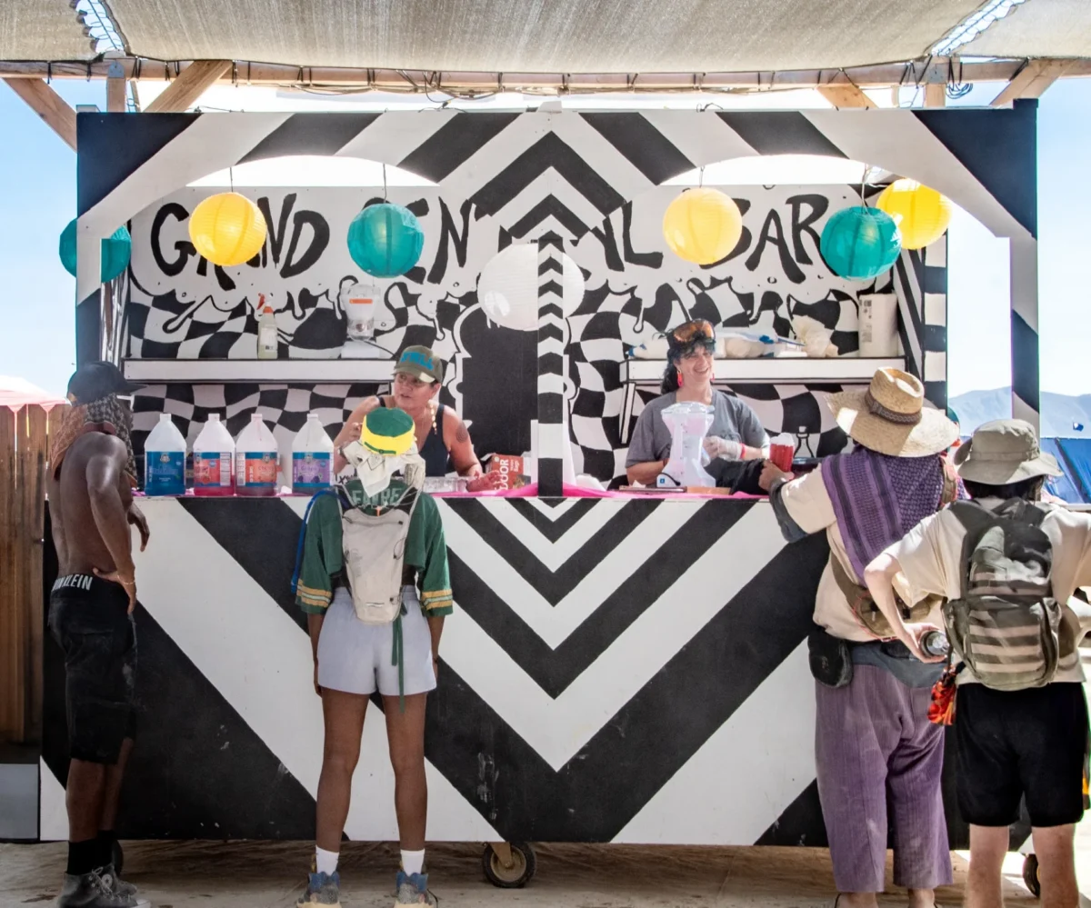 People stand at a counter with a sign 'Grand Central Bar' where people are gifting snow cones.