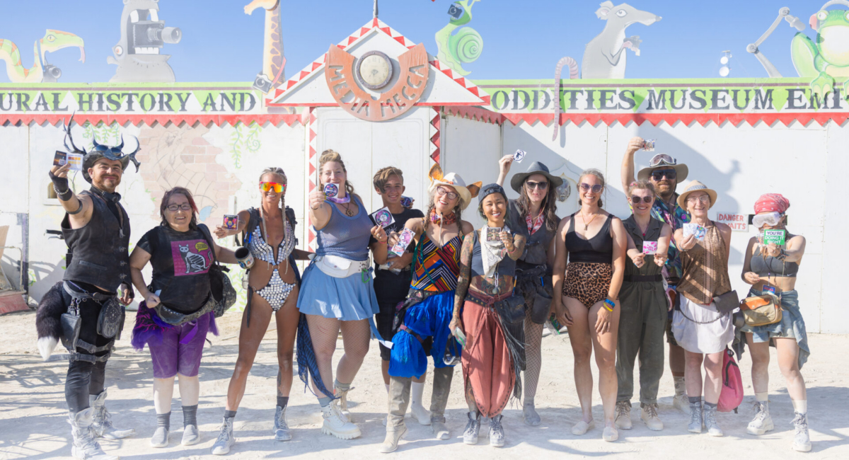 A dozen people stand in front of Media Mecca, holding different stickers towards the camera