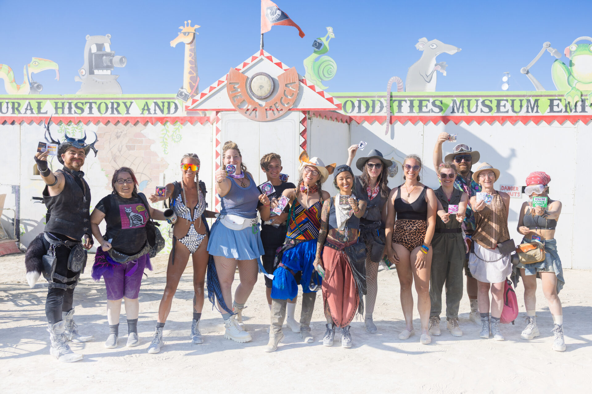 A dozen people stand in front of Media Mecca, holding different stickers towards the camera