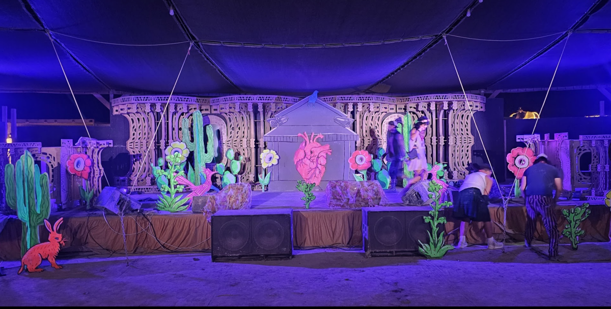 Blacklights illuminate a stage set decorated with painted wood and cardboard cacti and flowers.