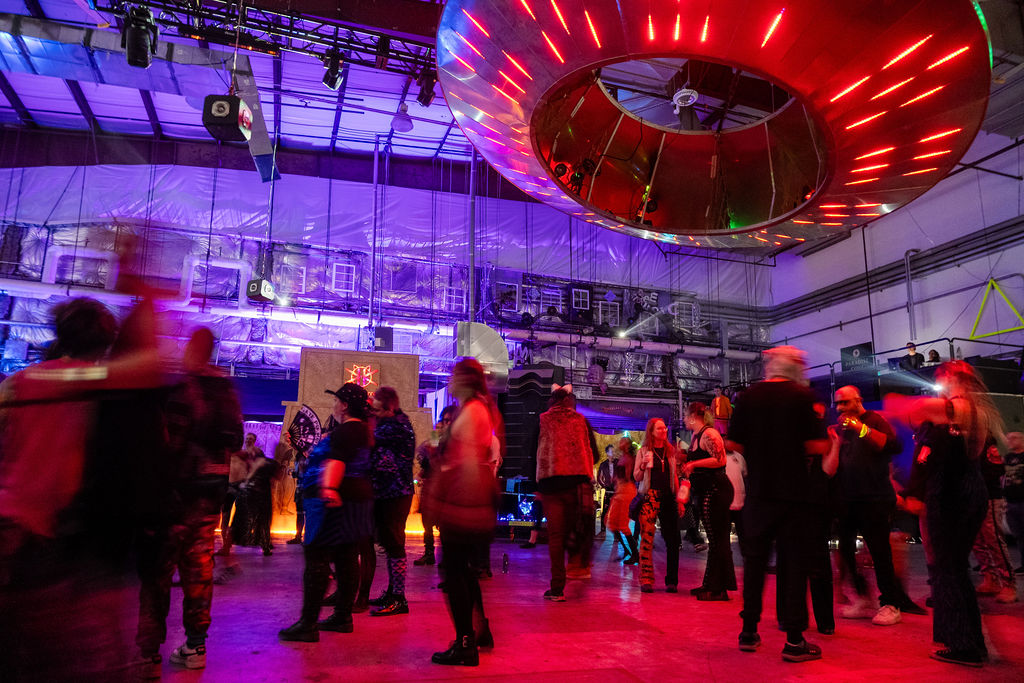 group of people standing and dancing in warehouse under lit up donut shaped lighting