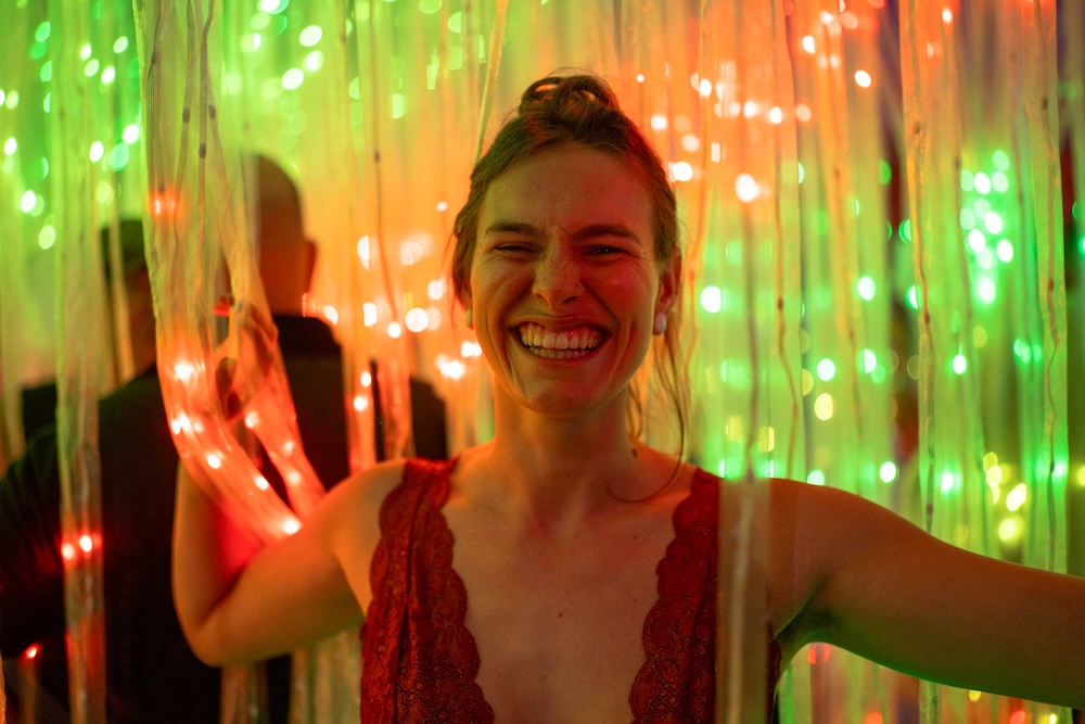 A smiling woman passes through dangling strands of lights