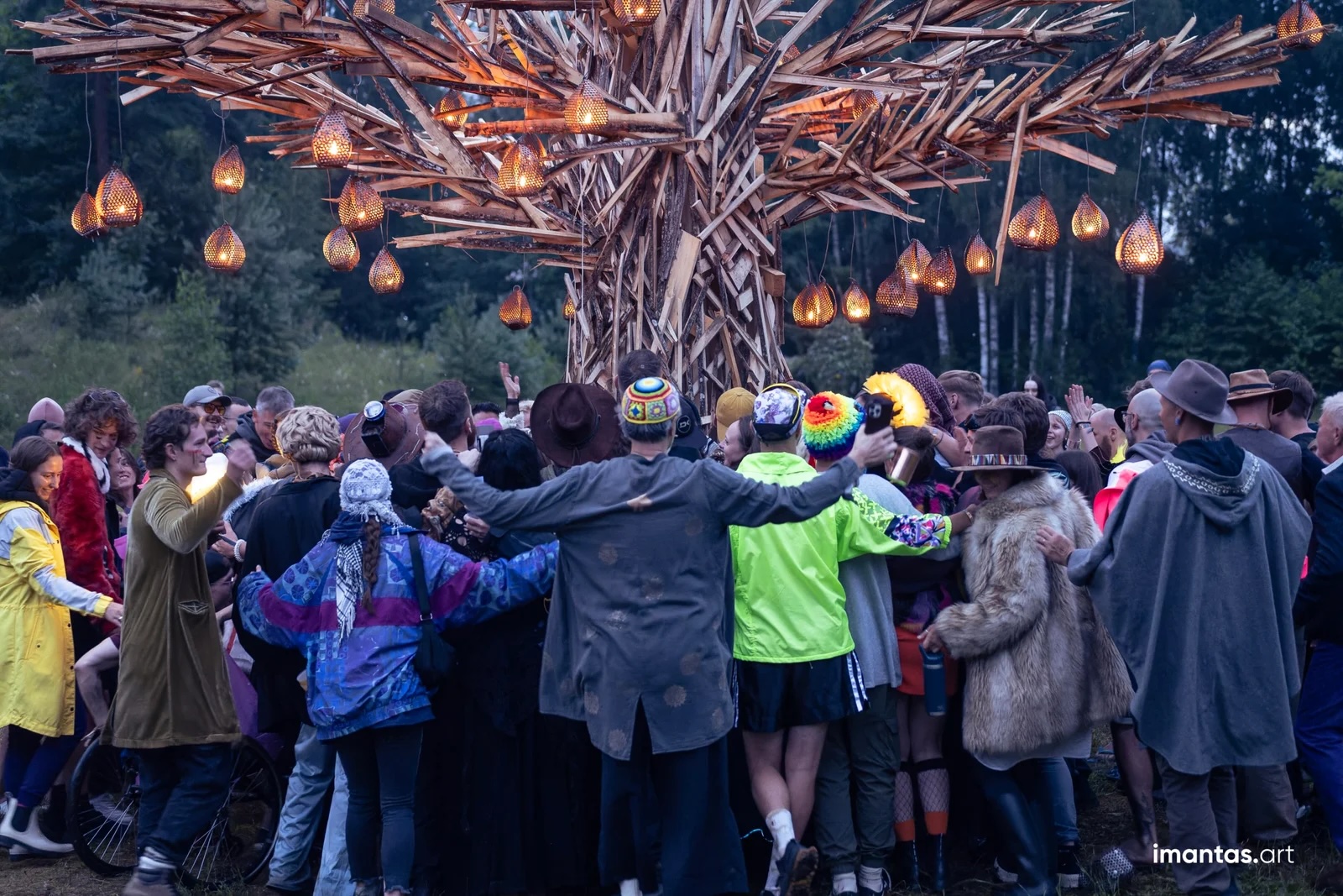 A group of people with arms around each others shoulders under a tree hung with glowing lanterns