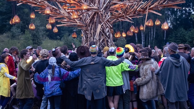 Group of people with arms around each other encircle a tree with lanterns dangling from it.