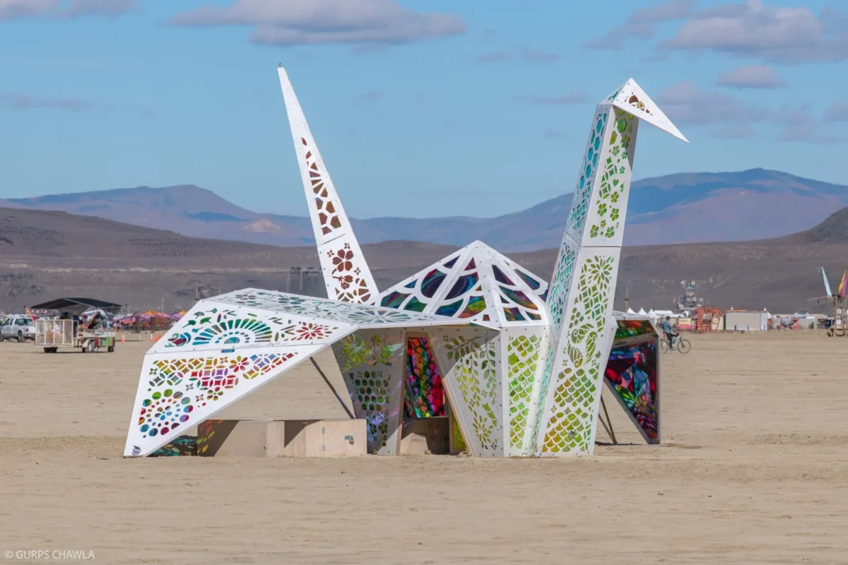 A paper crane sculpture large enough to stand inside with geometric shapes cut in the surface to expose colorful stained glass panels. 