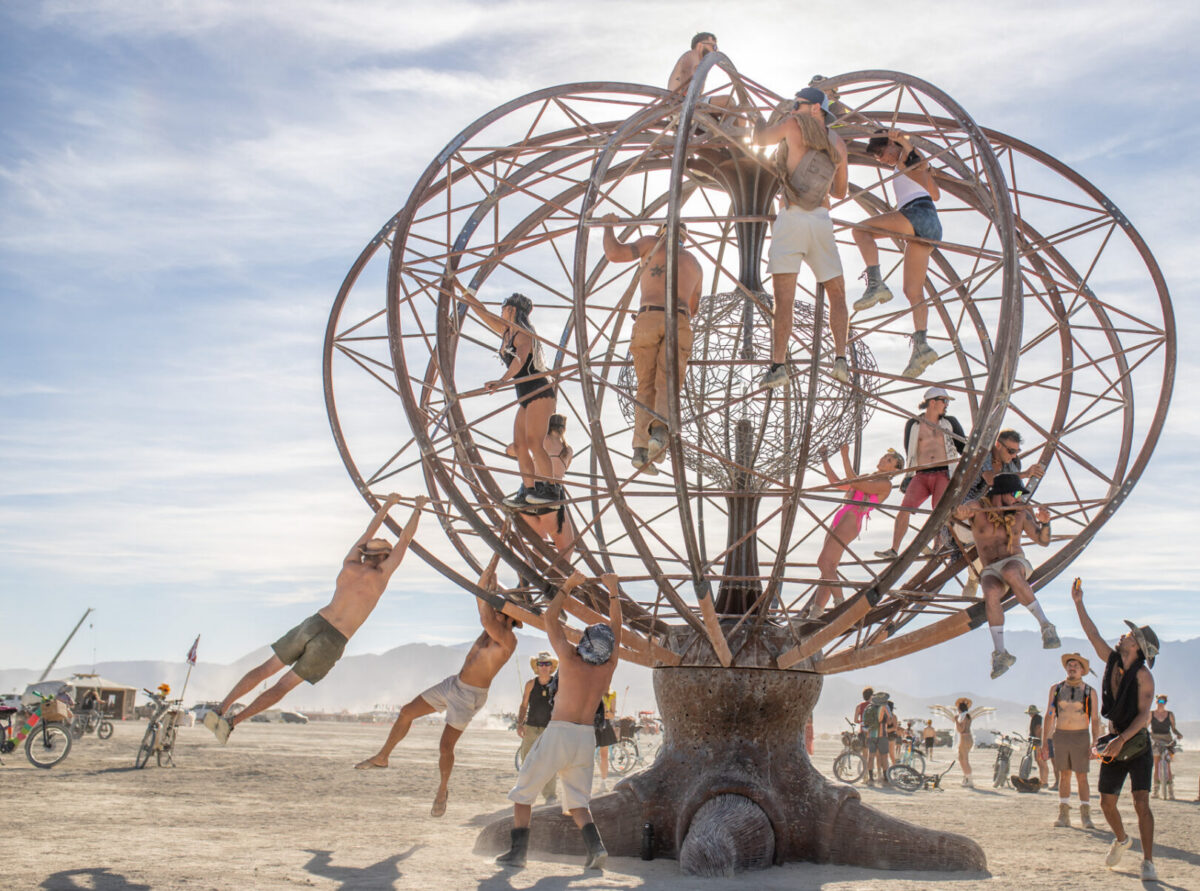 Adults climbing on and hanging from a sculpture together.
